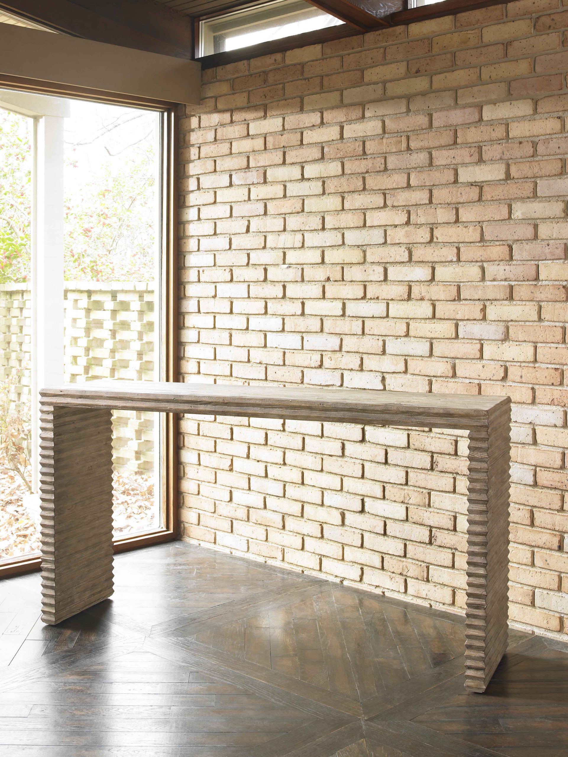 The Belmont Console in White Rustic Pine sits in front of a natural brick wall and bright window.